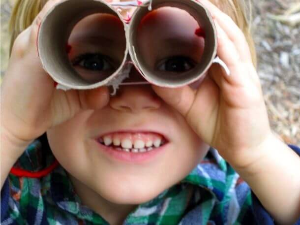 Boy smiling and looking through cardboard toy binoculars.