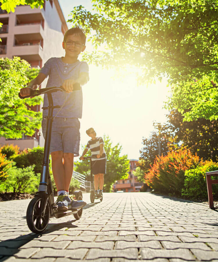 Young child riding a scooter in a green city.