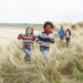 two kids running on beach sand dunes and parents trailing behind
