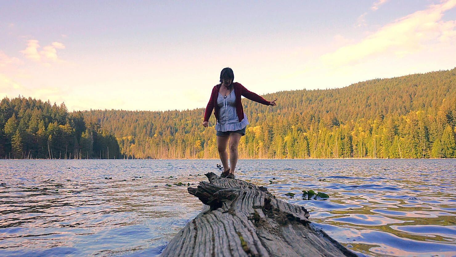 person walking on log on a lake