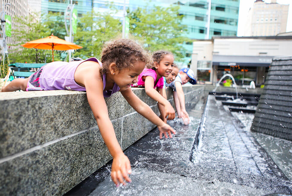 Kids splashing in a fountain in a city.