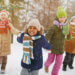 group of children in winter gear and snow holding hands running towards the camera together