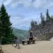 A mountain biker takes a break, sitting on a bench and looking out at a mountain valley.