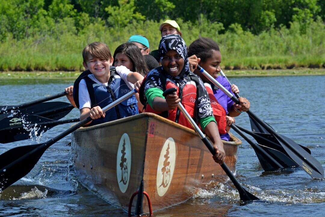 Group of kids paddling in a canoe.