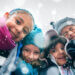 Kids together in winter clothes smiling during a snowfall.